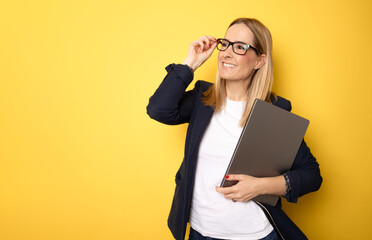 Wall Mural - Young business woman holding laptop computer and looking side over yellow background