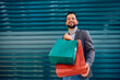 Young happy man with shopping bags looking at camera.