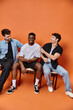 © LIGHTFIELD STUDIOS - jolly interracial men in casual street outfits smiling happily on orange backdrop, fashion concept