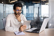 Concentrated and serious young Indian man working in office at desk with tablet