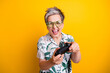 Photo portrait of nice pensioner lady hold joystick enjoy playstation wear trendy tropical print outfit isolated on yellow color background