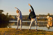 © Studio Romantic - Senior family duo stretching in nature. Happy healthy old couple in sportswear standing on grassy lake bank, doing side bend exercise, with beautiful landscape view background. Sports workout concept