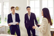 © Studio Romantic - Team of business people having a work meeting. Group of young corporate employees standing in the office and having a discussion. Male employees listening to a woman manager talking about teamwork