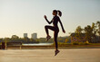Woman with a slim sporty figure having an outdoor fitness workout on a city street. Side view of a fit healthy young girl in a sports suit, with a ponytail doing a high knee jump exercise