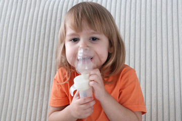 A little girl, a child of European appearance, blond hair, sits in an inhaler mask. Treatment of seasonal diseases with a nebulizer at home.