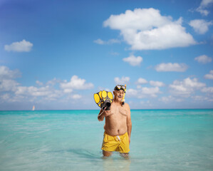 Mature man in swimming shorts holding snorkeling fins in the sea