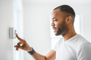 man choosing temperature on thermostat. Young focused guy pushing button home system.