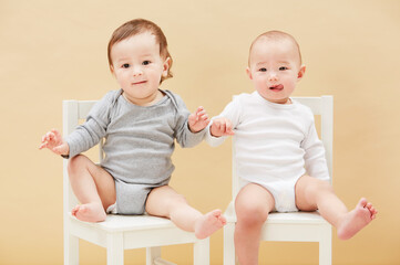 Portrait, chair and baby boys for growth or child development in studio on an orange background. Children, cute or adorable and sibling or small infant kids sitting together for family bonding