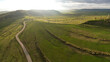 Aerial drone flight above a rural region in Transylvania at sunset. Grassy hills, sheep flocks, farms, storm clouds and sunlight create a beautiful countryside landscape. Romania