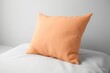 © Friedbert - An orange pillow sitting on top of a white bed, peach fuzz, trendy color of the year 2024.
