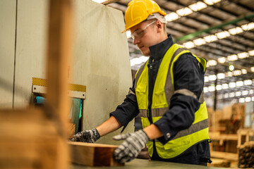 man cleaning timber wood in dark warehouse industry. Team worker carpenter wearing safety uniform and hard hat working and checking the quality of wooden products at workshop manufacturing.