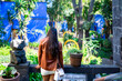 Unrecognizable young Latin woman tourist in casual clothes standing in garden at Blue House of Frida Kahlo Museum of Mexico City while admiring green plants on sunny day