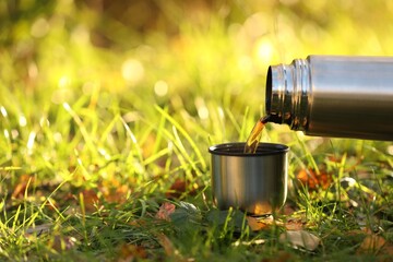 Canvas Print - Pouring tea from thermos into cup lid on green grass outdoors, closeup. Space for text