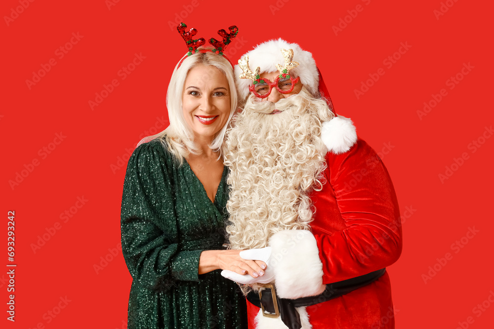 Santa Claus and beautiful mature woman in Christmas deer horns on red background