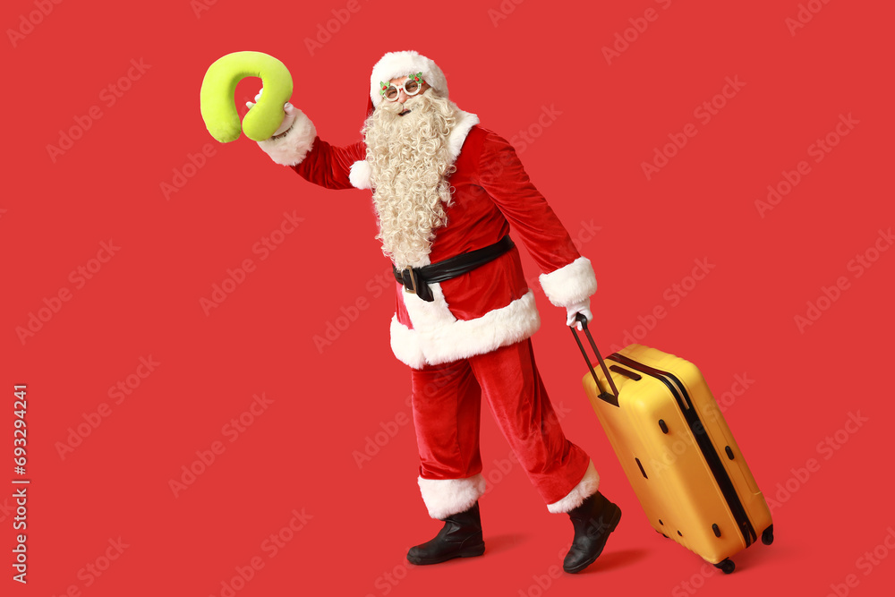 Santa Claus with suitcase and travel pillow on red background. Christmas vacation concept