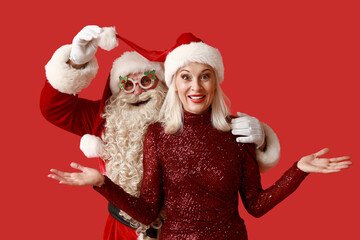 Sticker - Santa Claus with beautiful mature woman in Christmas glasses and hats on red background