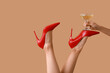 Female legs in high heel shoes with glass of champagne on beige background. New year party concept