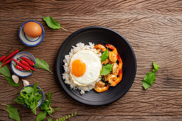 Sticker - Stir-fried shrimp with basil Thai street food arranged on a black plate with a fried egg Spicy Thai food placed on a wooden table. Top view.