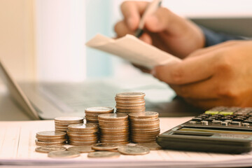 Accountant working on desk using calculator with coins placed next to the concept of calculating financial reports, calculating taxes, income and expenses Calculate numbers for your organization