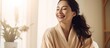 Happy young Asian woman in silk bathrobe enjoying morning beauty routine at home, applying face care product and smiling, with space for copying.