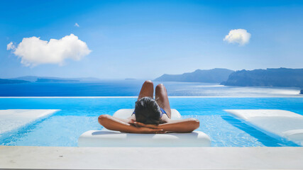 Wall Mural - Young Asian women on vacation at Santorini relaxing in a swimming pool looking out over the Caldera ocean of Santorini, Oia Greece, Greek Island Aegean Cyclades during summer in Europe