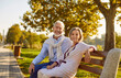 © Studio Romantic - Portrait of happy married senior couple in beautiful green park on good sunny summer day. Cheerful old man and woman in smart casual clothes sitting on bench together, looking at camera and smiling