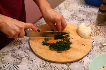 Crop anonymous female chef in uniform cutting fresh green parsley with knife on cutting board in kitchen