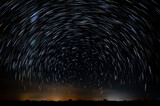 Fototapeta  - Abstract photo of Blue Night sky star trail background.Startrails on a dark blue sky at night,center sky area.Rotating star lines. The North Star and meteor showers.