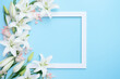 white lily flowers around a plain blank white frame plain blue background for greeting, announcement card