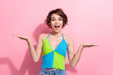 Portrait of amazed funny young girl hold two open palms demonstrating novelty product wear crop top isolated pink color background