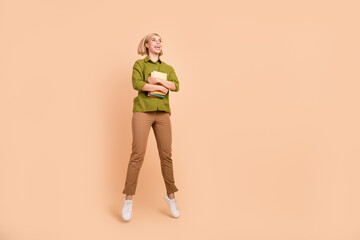 Wall Mural - Full size photo of ecstatic girl wear khaki shirt hold book fly staring at proposition empty space isolated on pastel color background