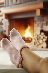 Wall Mural - Woman legs with warm socks and home interior with fireplace. 