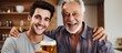 © AkuAku - Adult son and senior father celebrating with beer at home in cropped image.