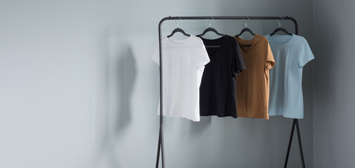 Sticker - T-shirts of neutral colors on  black hanger against  gray wall