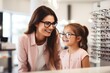 Smiling girl trying glasses with oculist, blurred mother in optics storecopy space for text.