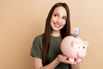 Sticker - Portrait of dreamy mature woman hold piggy bank looking curious novelty puts banknote inside box isolated on beige color background