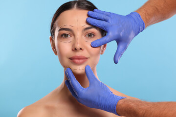 Canvas Print - Doctor checking marks on woman's face for cosmetic surgery operation against light blue background