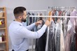 Dry-cleaning service. Worker choosing clothes from rack indoors