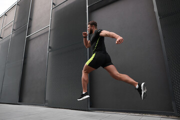 Canvas Print - Man running near building outdoors, low angle view. Space for text