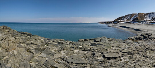 Wall Mural - Russia. The Far East, the Kuril Islands. View of the cold expanse of the Sea of Okhotsk against the background of snow-capped volcanoes surrounded by basalt rocks.