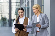 © Liubomir - Two business women are walking outside the office center with a tablet and documents in their hands and discussing work matters.
