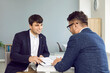 © Studio Romantic - Two young men business partners in office sign contract sitting at desk, manager gives document to his client. Business meeting, transaction, conclusion of contract, provision of services concept.