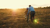 Fototapeta  - Affectionate papa actively involved in assisting little kid on riding bicycle. Caring dad prevents mishaps holding bike of son. Father provides risk-free bike ride for beloved child in field
