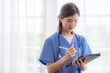 © ultramansk - Asian Female medical assistant with smart tablet in white background. Portrait of mature female nurse working in hospital. Woman healthcare worker. Portrait of a good looking young nurse.