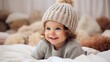 © venusvi - Happy little child wearing a stylish knitted hat lies on the bed