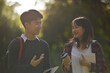 Backlit photograph of two Asian students talking while walking in a park
