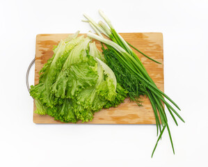 Wall Mural - Green salad, green onions and bunch of dill on a wooden cutting board. Side view. Fragrant greens.