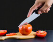 © Merlin - hand use knife to slice tomato isolated in black background
