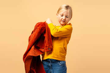 Wall Mural - Cute focused little girl wearing brown jacket while preparing go to school isolated beige background. Childhood concept