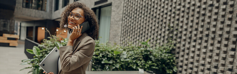 Pretty female freelancer is talking phone with client while standing on coworking background